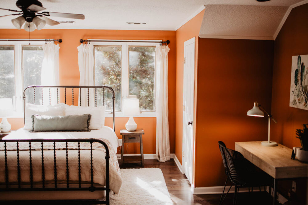 A warm and inviting bedroom in a WinShape Group Home featuring a metal bed frame, rust-colored walls, and a wooden desk.