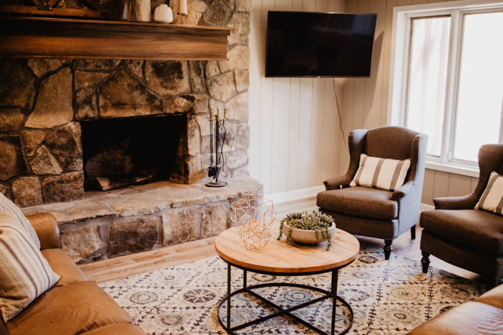 Warm and comfortable group home living room featuring a large stone fireplace, cozy armchairs, and a patterned area rug.