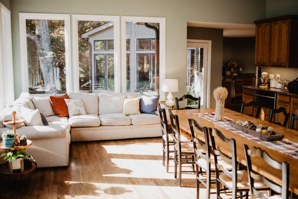 Bright, open-concept living space and dining area with large sofa next to a long wooden dining table.