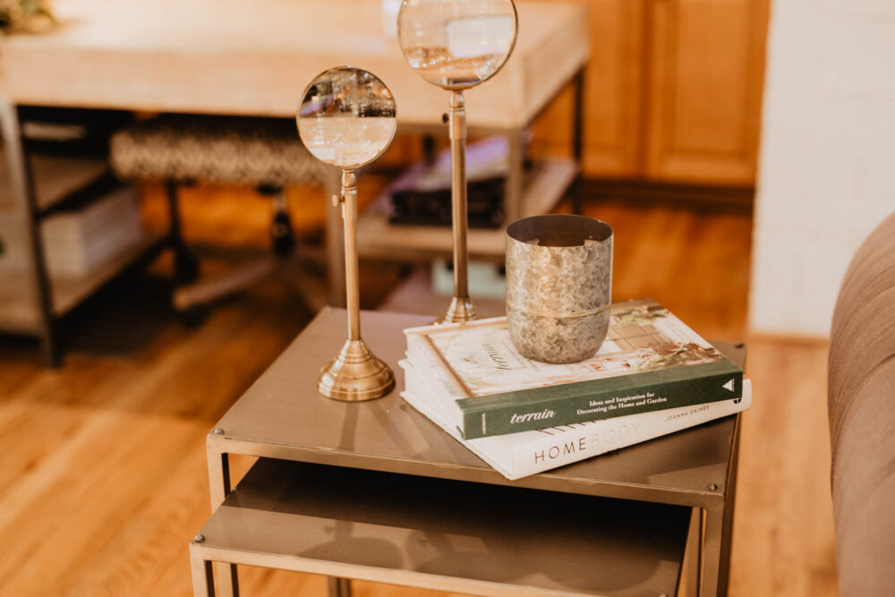 Close-up of modern decorative items on a nesting side table, including magnifying glasses, a candle, and interior design books.