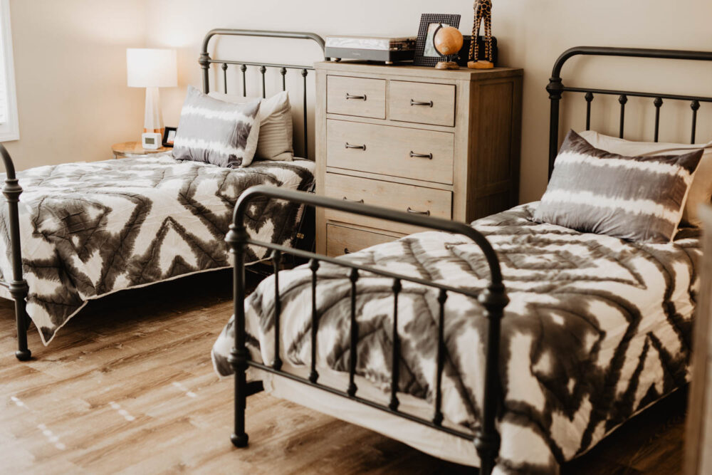 A shared bedroom in a group home with two twin beds featuring black metal frames and matching gray and white patterned bedding.