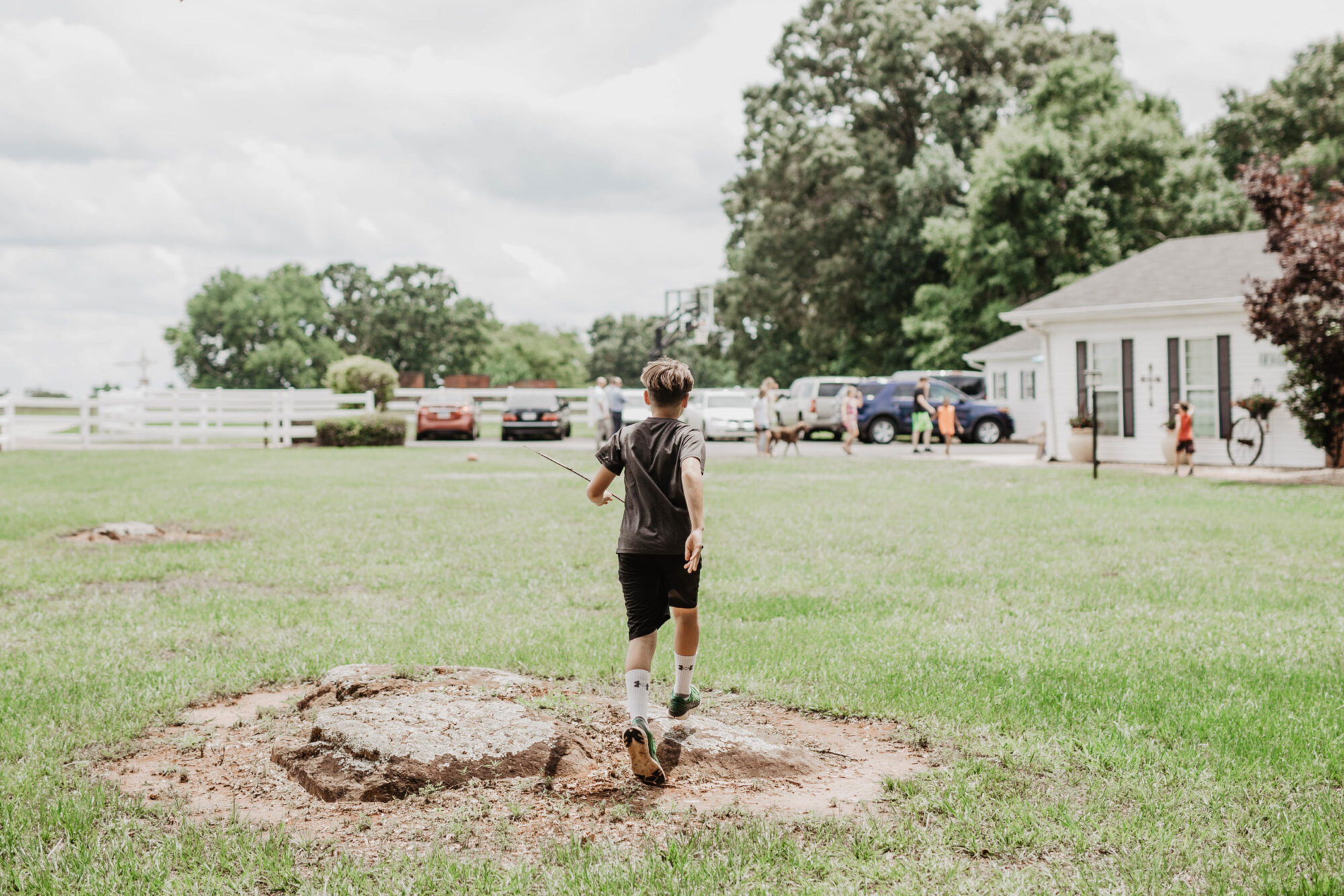 A boy in a grassy field running towards people and a house.