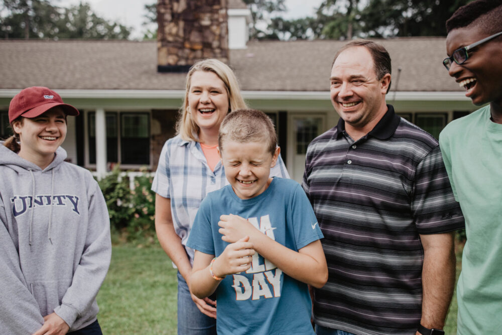 A diverse foster family laughing in front of a home.