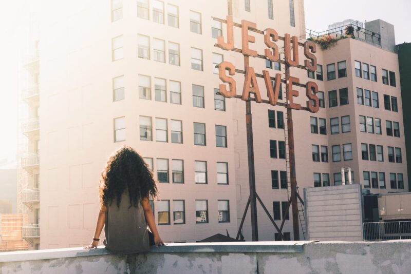 A girl sitting on building ledge looking at a sign that says 