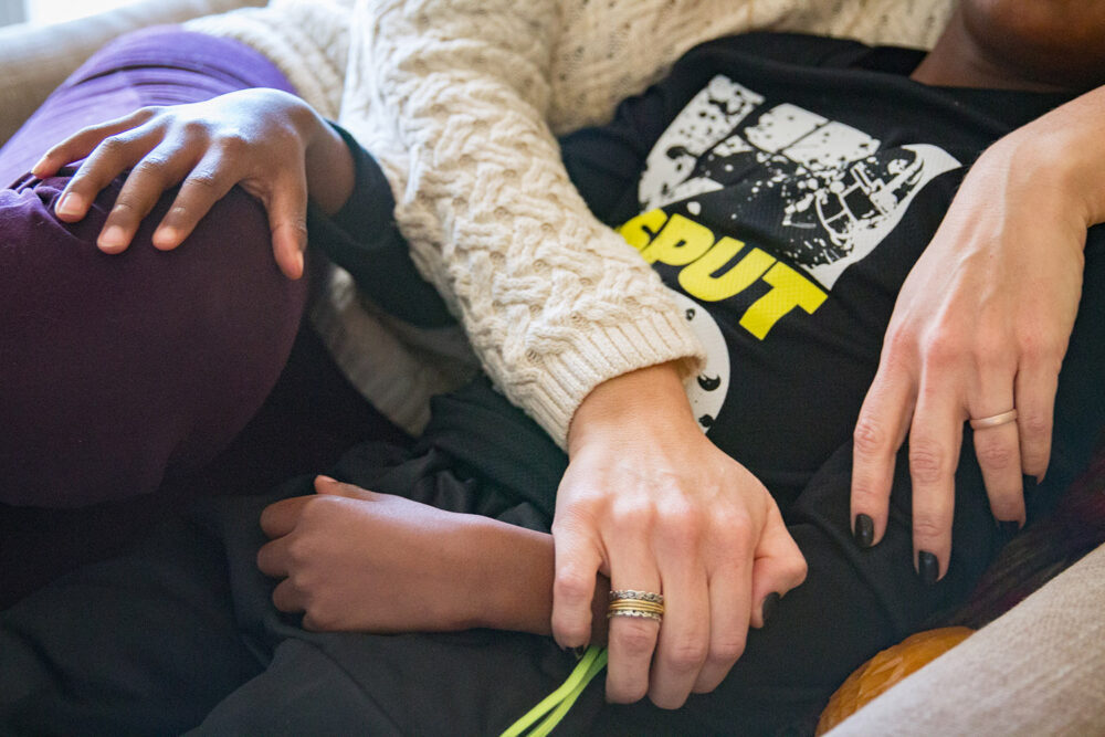 Close-up of three hands resting on two people's bodies.
