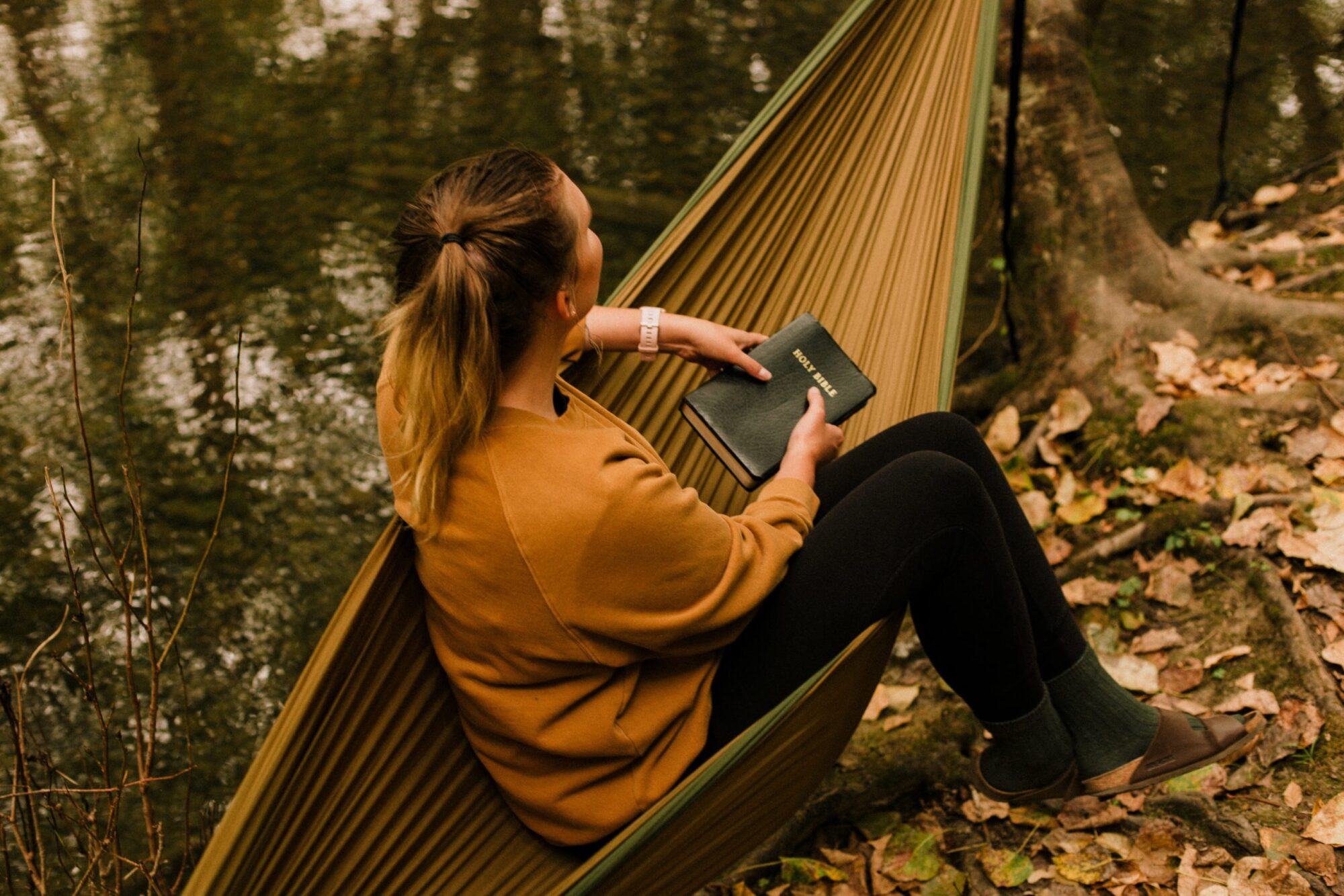 Woman sitting on a hammock with a Bible, practicing quiet time and self-care to renew your mind.