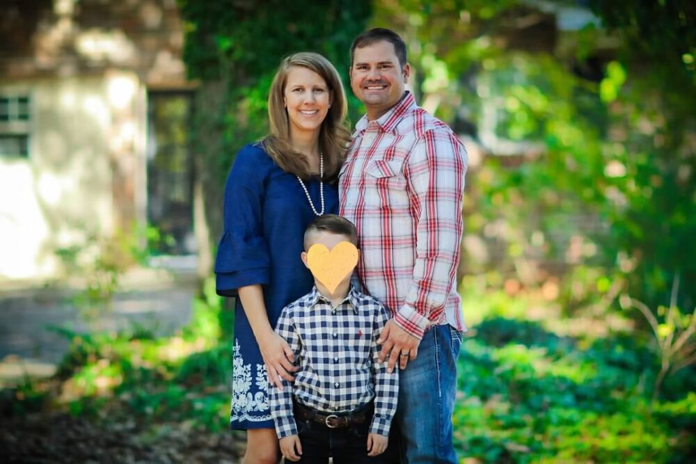 Two smiling parents holding there son with a heart over his face.