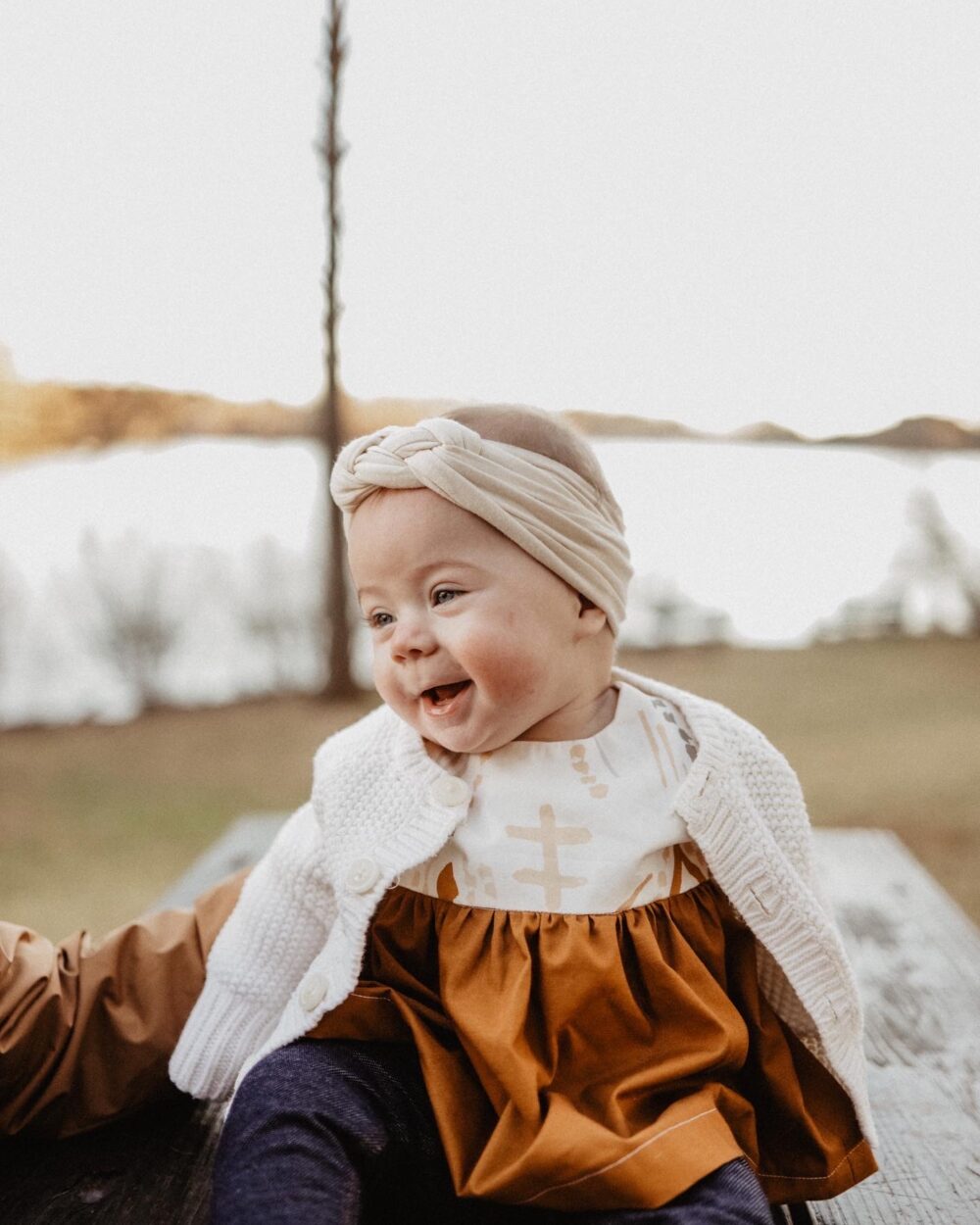 A baby smiling with a white and orange outfit on.