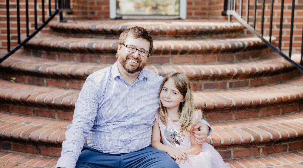 A father putting his arm around his daughter on brick stairs.