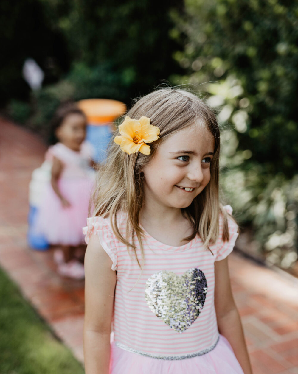 A girl with a flower in her hair and a pink striper heart shirt smiling.