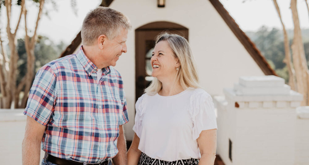 A man with a plaid shirt and woman with a white shirt smiling at each other.