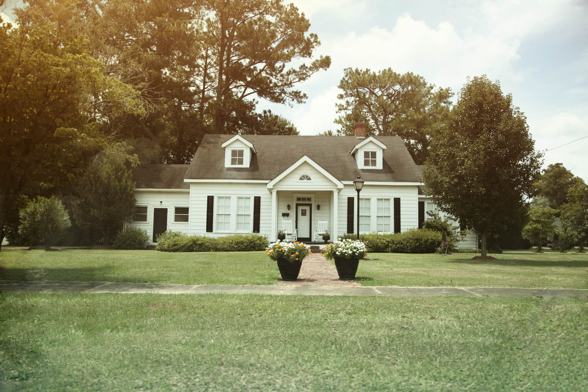 A white house surrounded by trees with two potted plants in front of it.