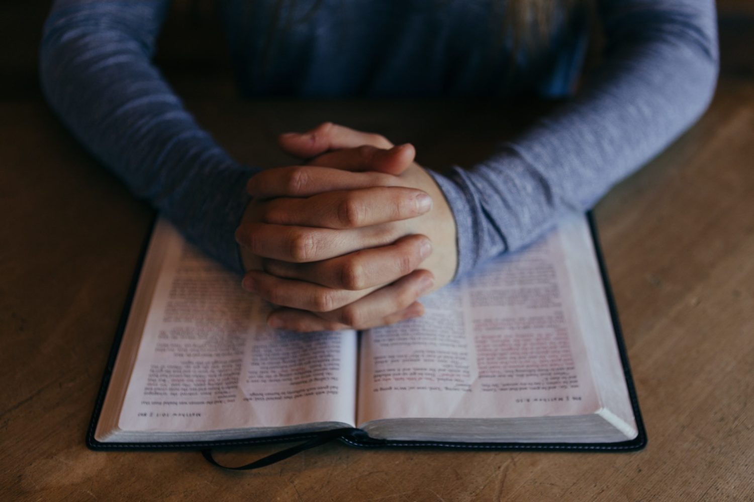 A close-up of a man locking his hands together on a bible.