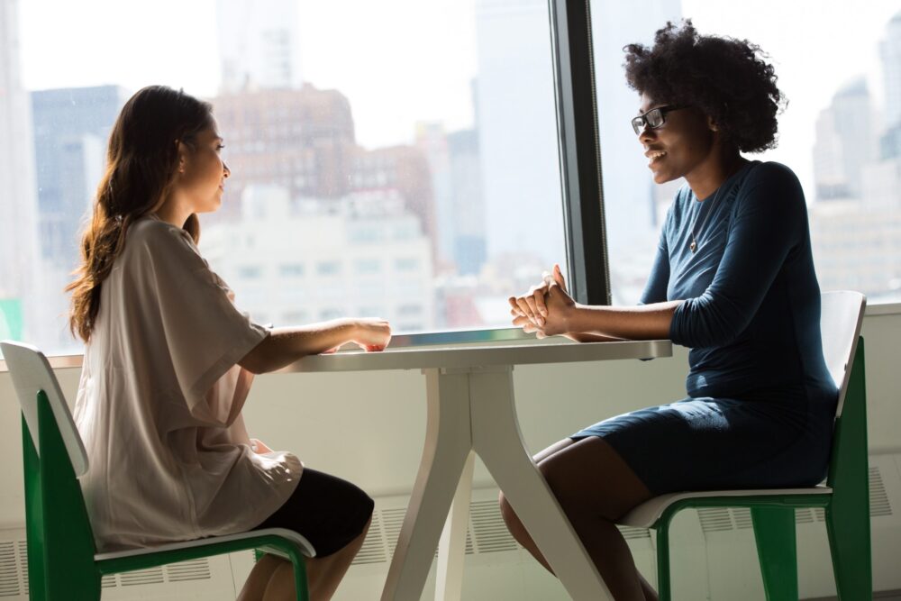 Two women sitting at a table next to window talking about foster care agency home study.