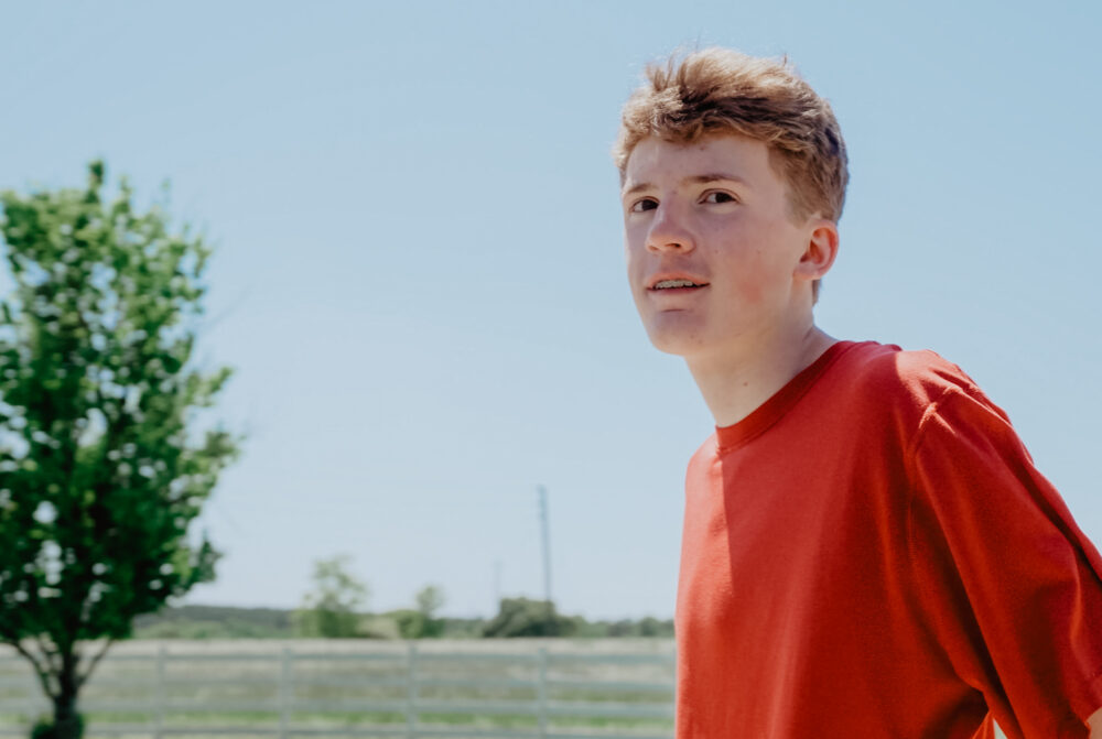 A foster teenager boy with a red shirt smiling.