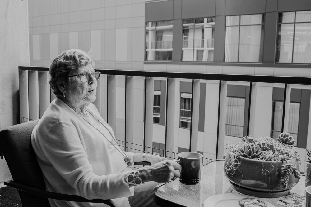 An black and white photo of an older woman sitting with her hand holding a mug.