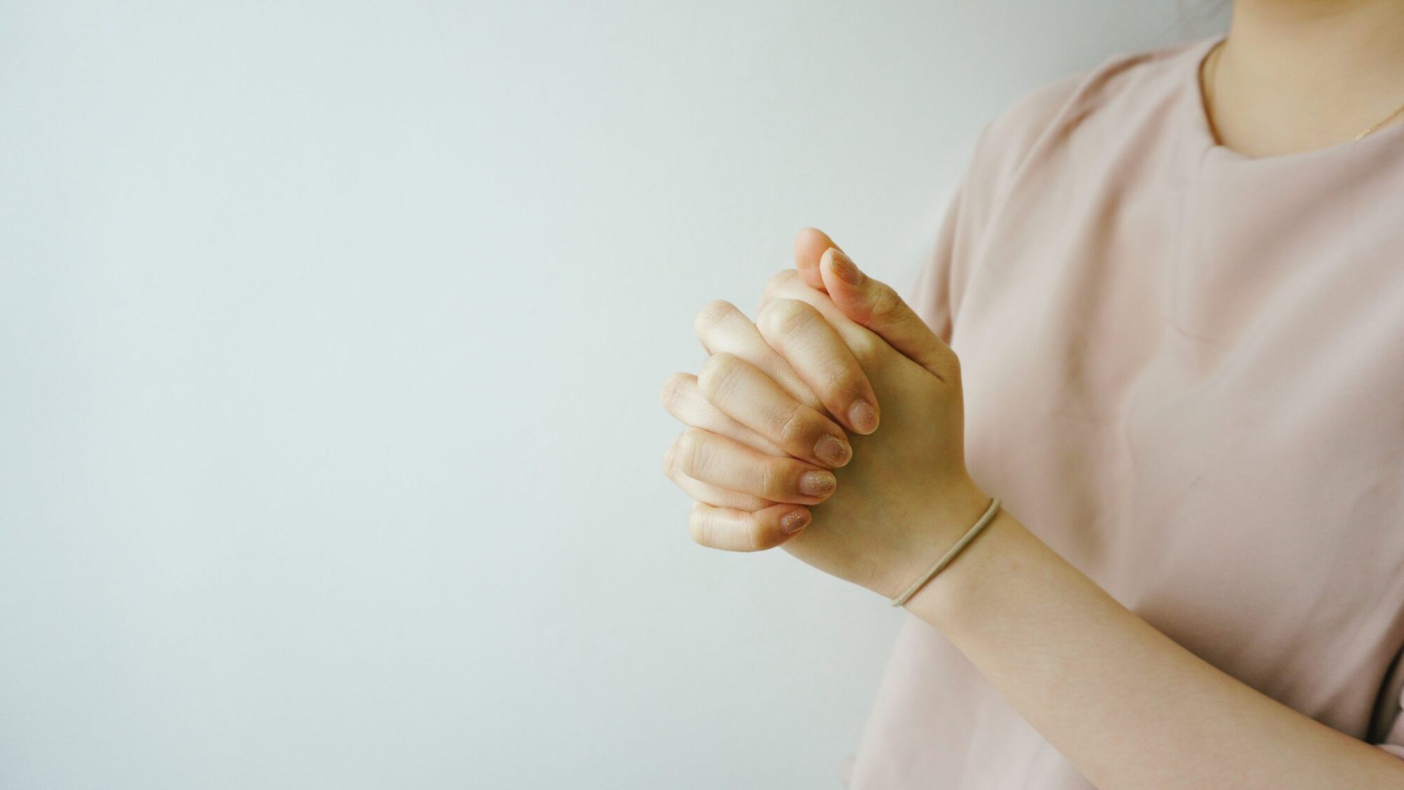 A close-up of a girl with pink locking hands together signifying prayer.