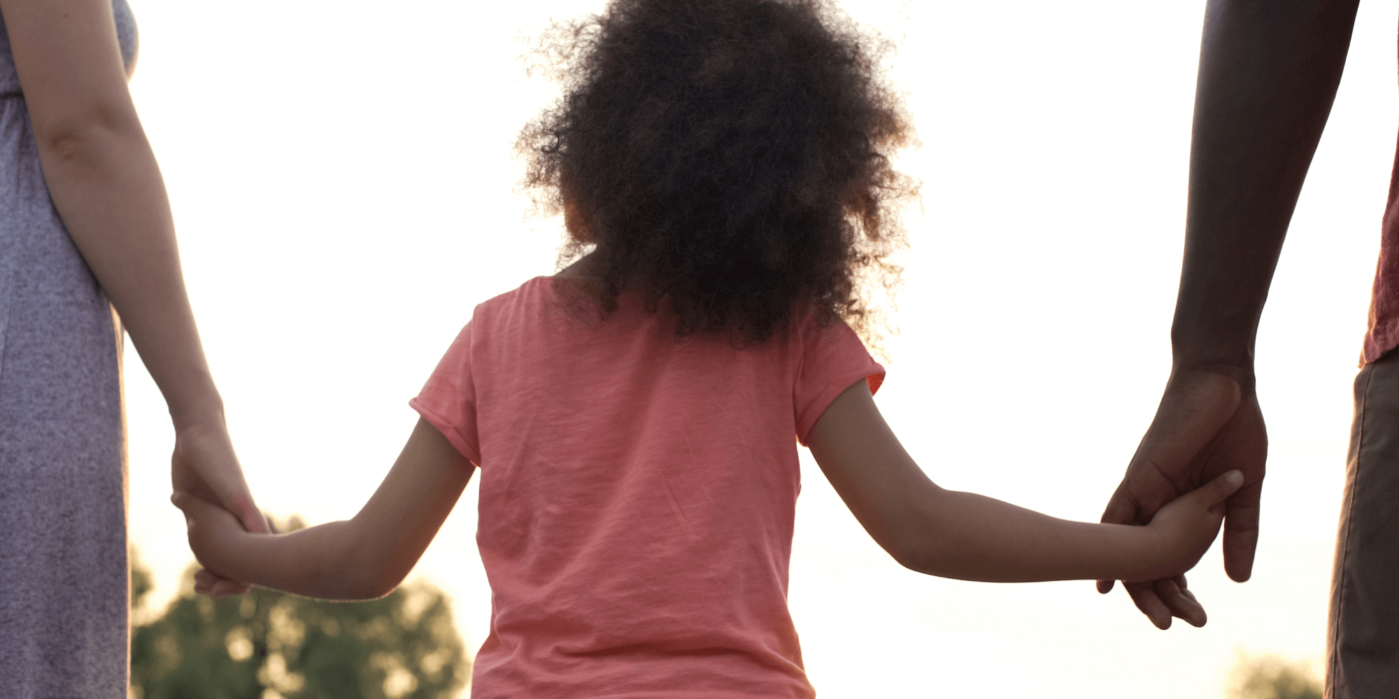 An afro girl holding hand with two adults.