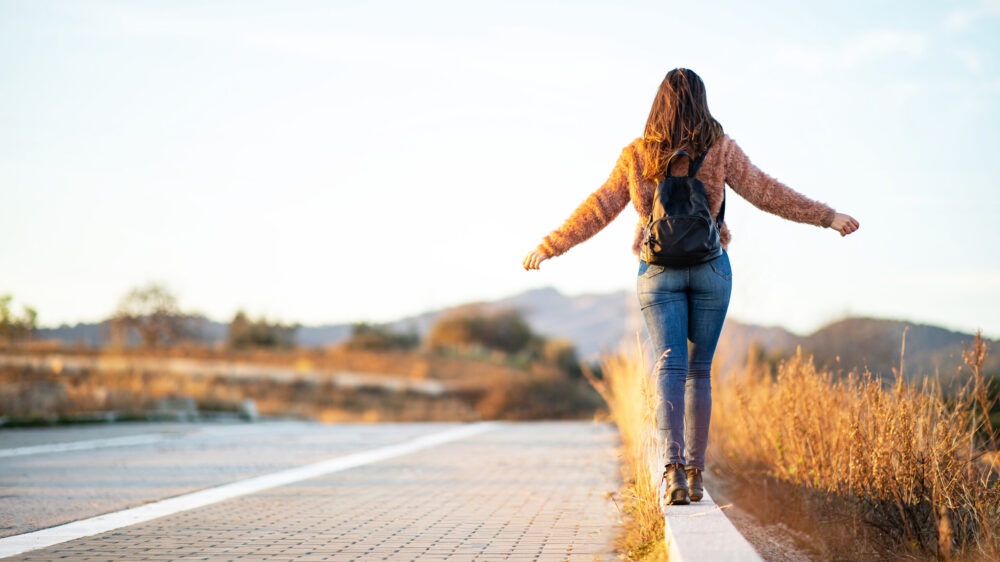 A girl with a backpack balancing on a curb.