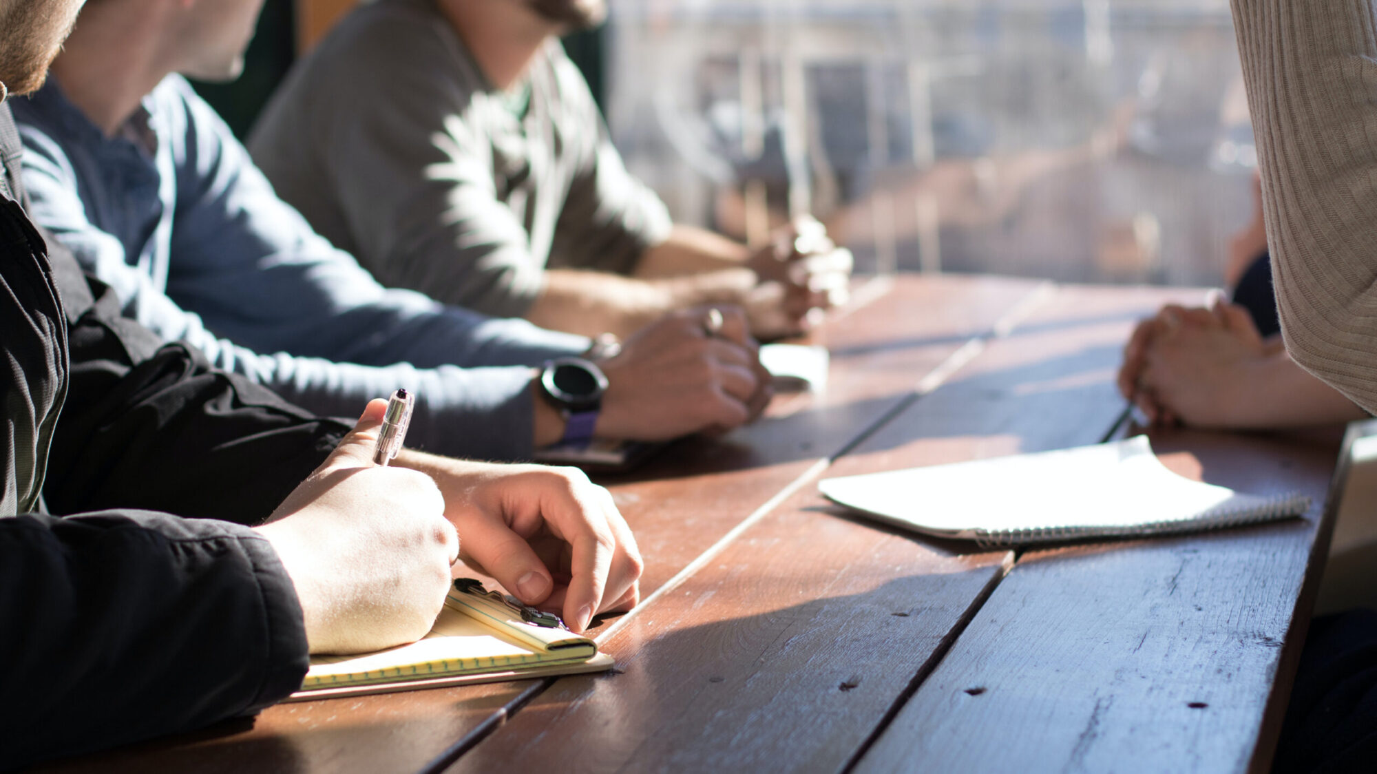 A focused group of people seated at a long wooden bench writing notes.