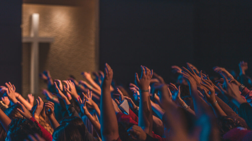 A lot of of hands being raised in air while worshiping in a church.