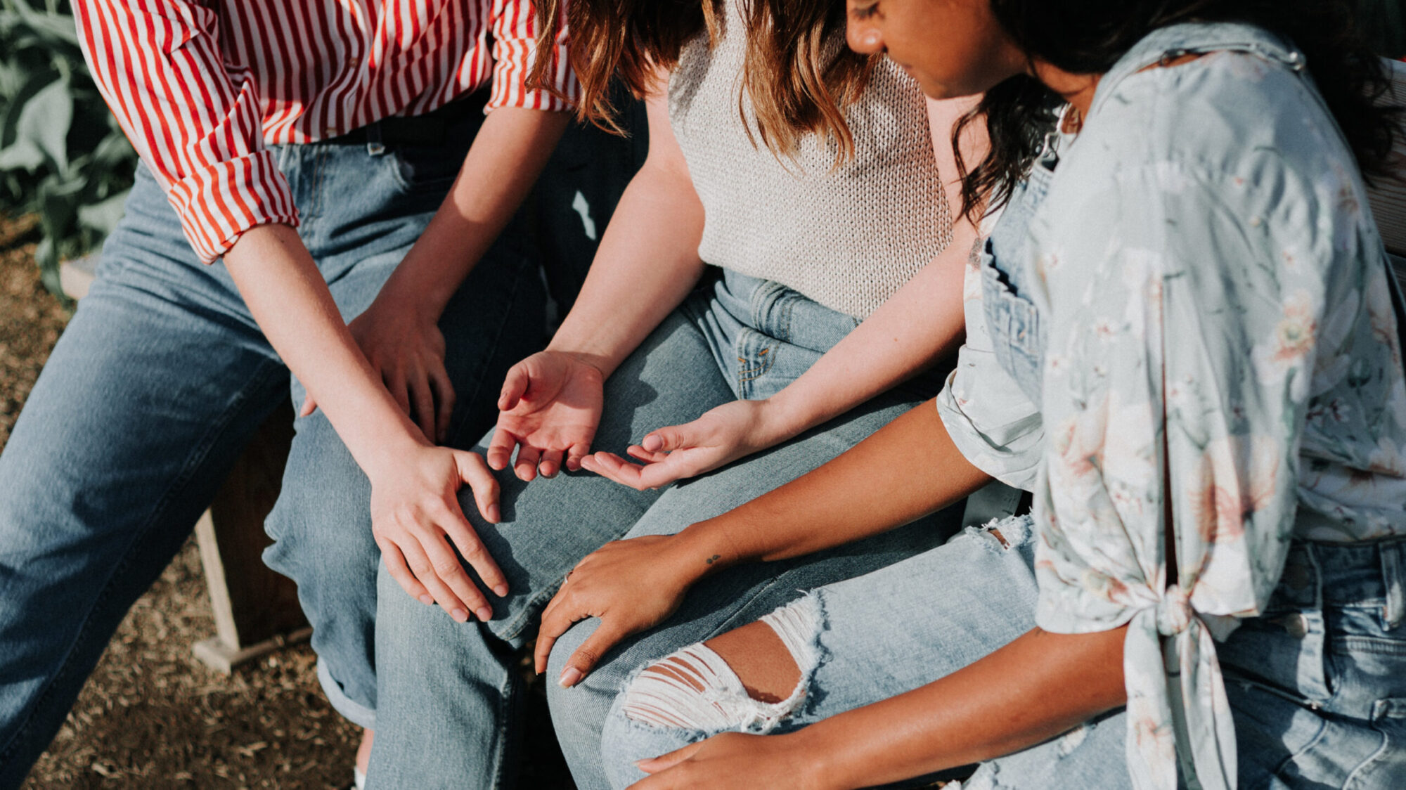 Three women praying for trauma-informed care while putting there hands on each others' knees.