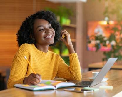 A girl in a bright yellow shirt smiling while writing in a book